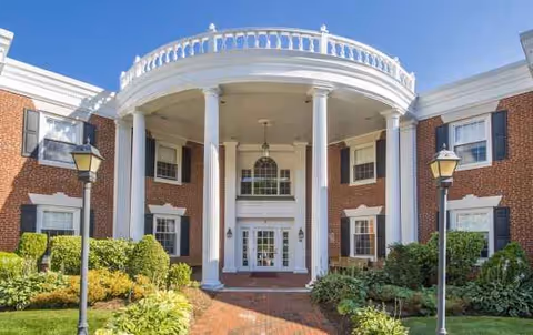 Brick senior living facility exterior with white columns and circular balcony.