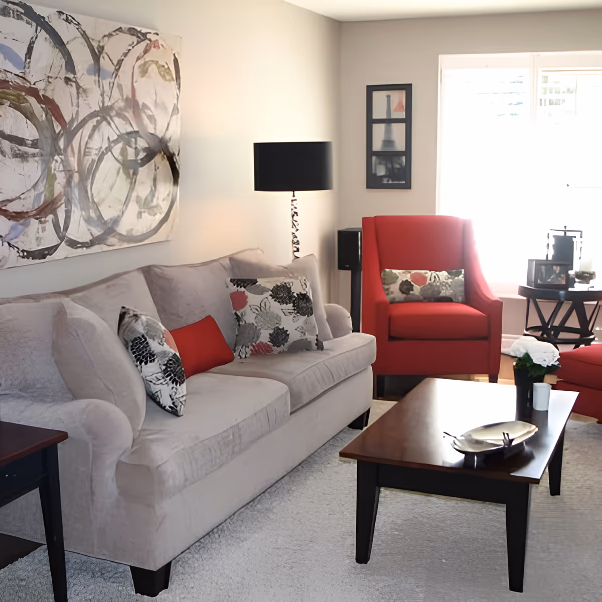A bright living room with a beige sofa, red armchairs, a wooden coffee table, and abstract wall art.
