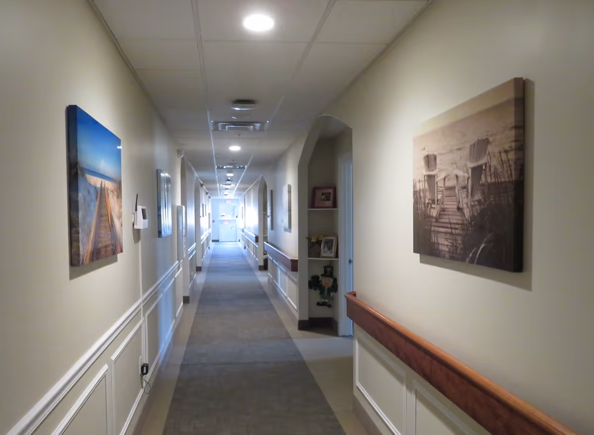 Long, well-lit interior hallway with handrails, carpet runner, and framed artwork on the walls.