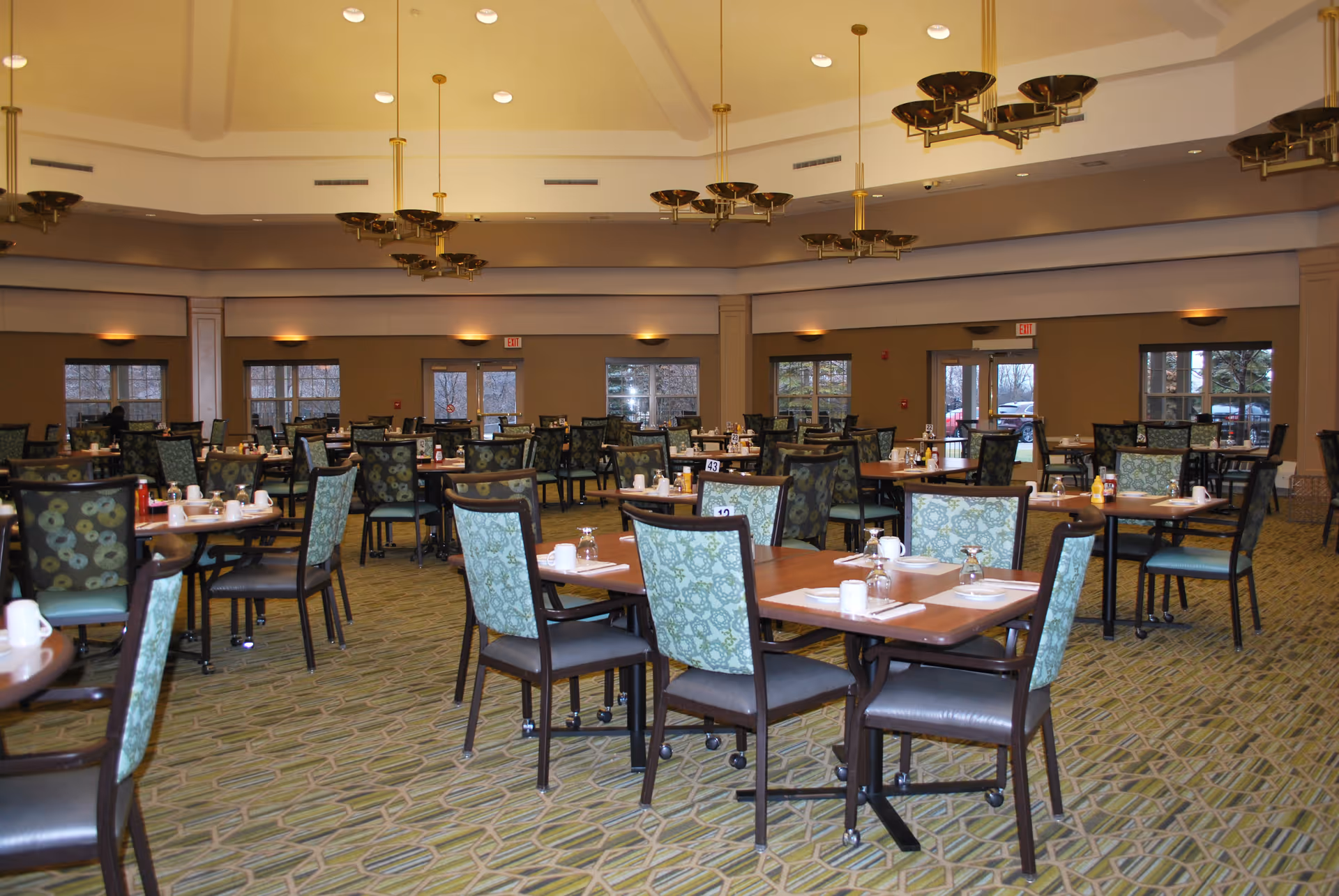 Spacious dining room with many set tables and patterned chairs arranged under chandeliers.