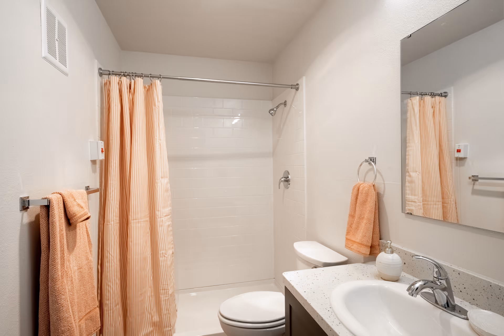 Clean bathroom with a shower-tub behind a peach-striped curtain, matching towels, toilet, and a sink with mirror.