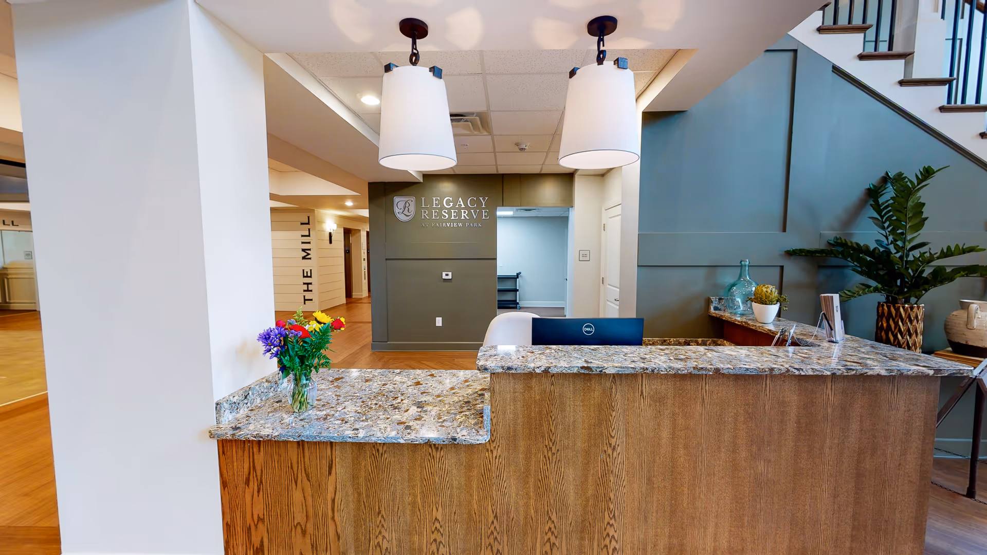 Reception desk with a granite countertop, vase of flowers, and a 'Legacy Reserve' sign on the back wall inside a facility lobby.