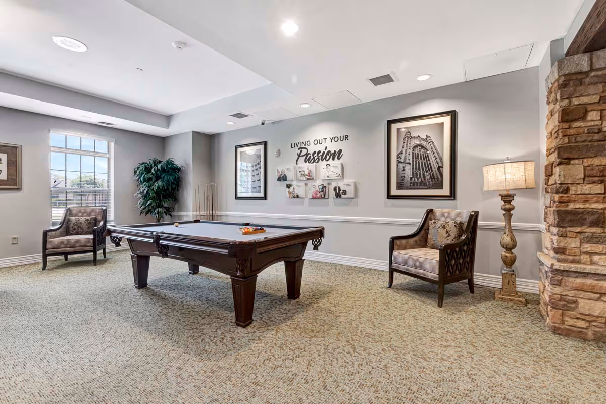 Bright recreation room with a pool table, two armchairs, framed artwork and a floor lamp.