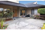 Exterior view of the entrance area of Park Rose Care Center featuring a covered walkway, large windows, a wooden bench, and landscaped plants and bushes.