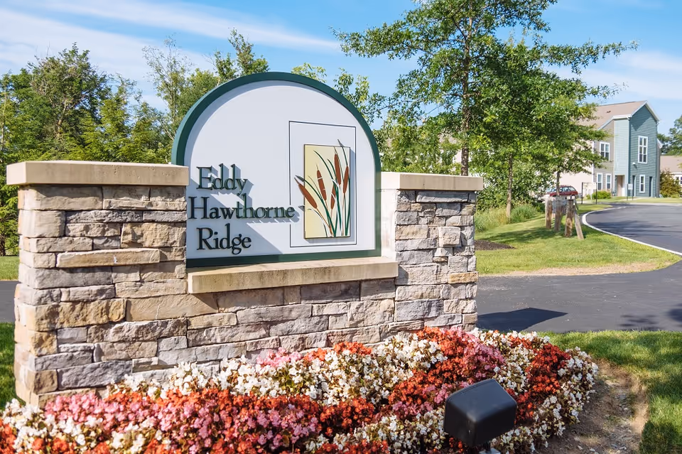 Stone entrance sign reading "Eddy Hawthorne Ridge" surrounded by flowers and landscaping with residential buildings in the background.