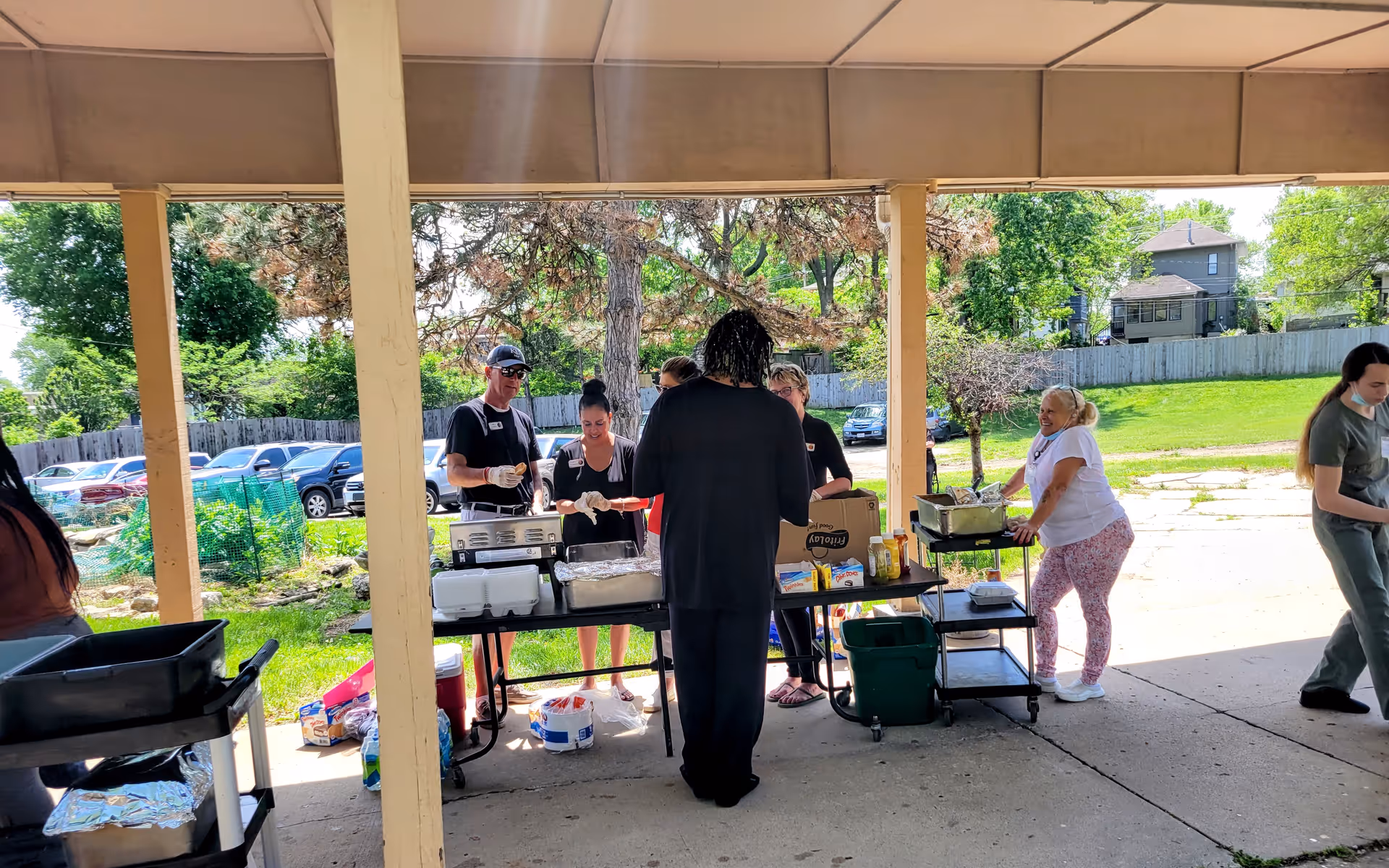 People gathered under a covered outdoor pavilion serving food from tables and carts.