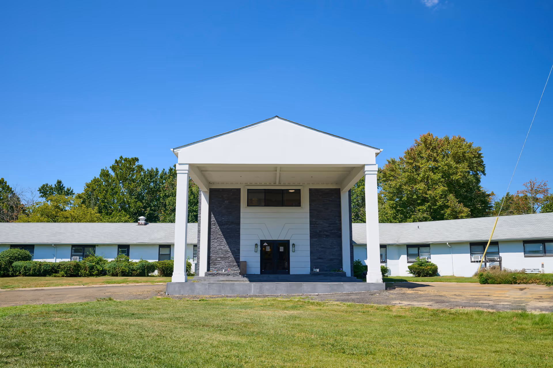 Front view of a white single-story building with a columned covered entrance and a grassy lawn.