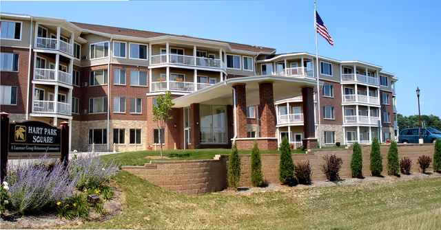 Exterior view of Hart Park Square Senior Living building with a canopy entrance and flag