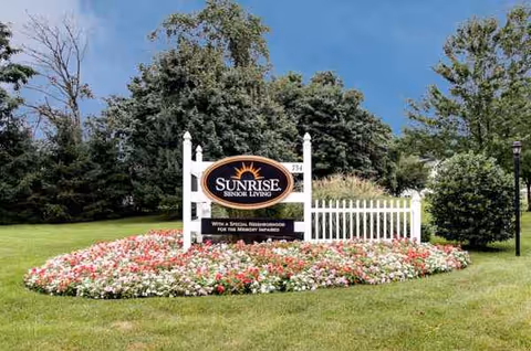 Sunrise Senior Living sign with white picket fence and colorful flower bed.