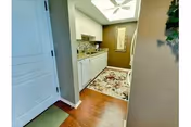 Small interior hallway leading to a kitchenette with white cabinets, a sink, a floral rug, and hardwood floors.
