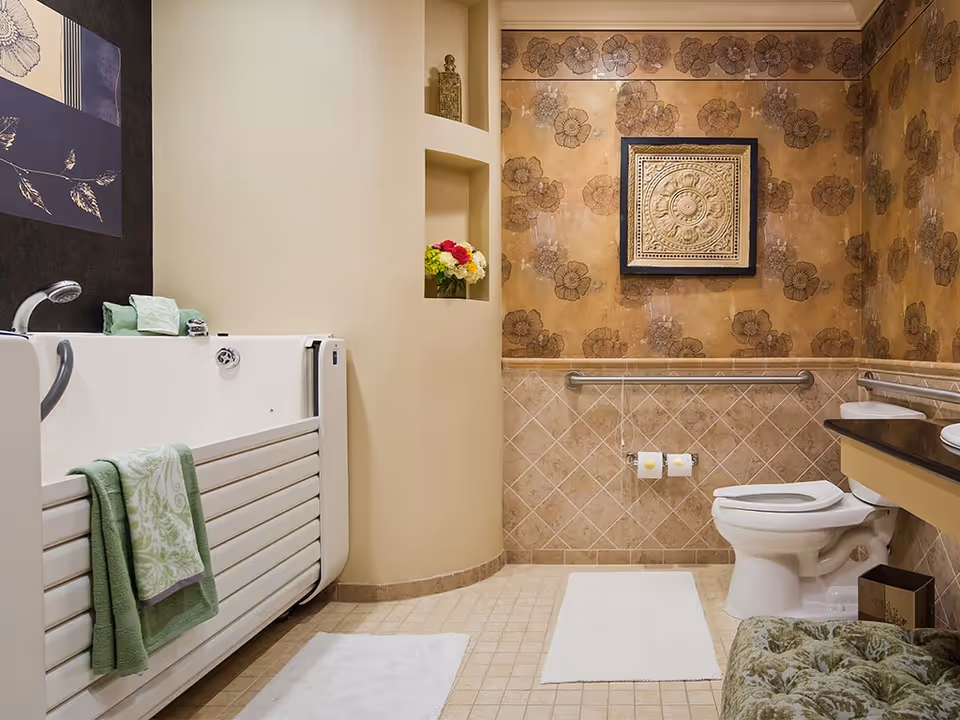 Accessible bathroom with a walk-in tub, toilet, grab bars, floral wallpaper and decorative wall art.