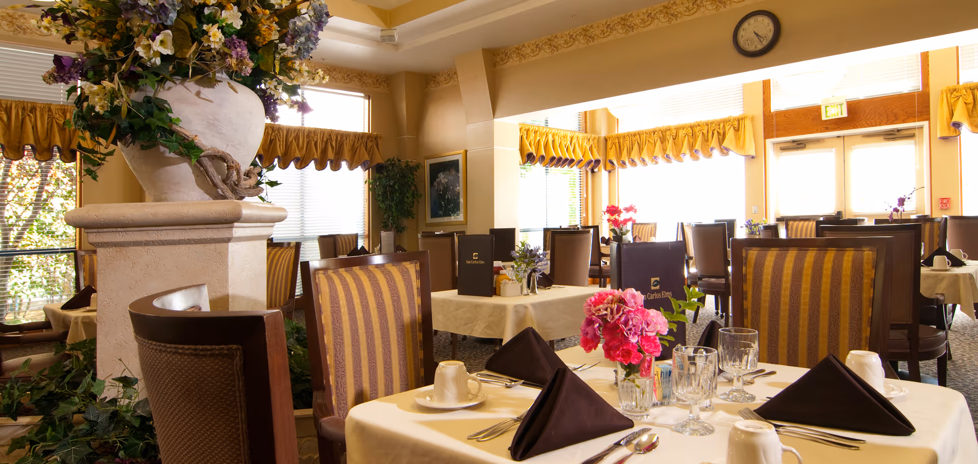 Bright, well-appointed dining room with set tables, floral centerpieces, and upholstered chairs.
