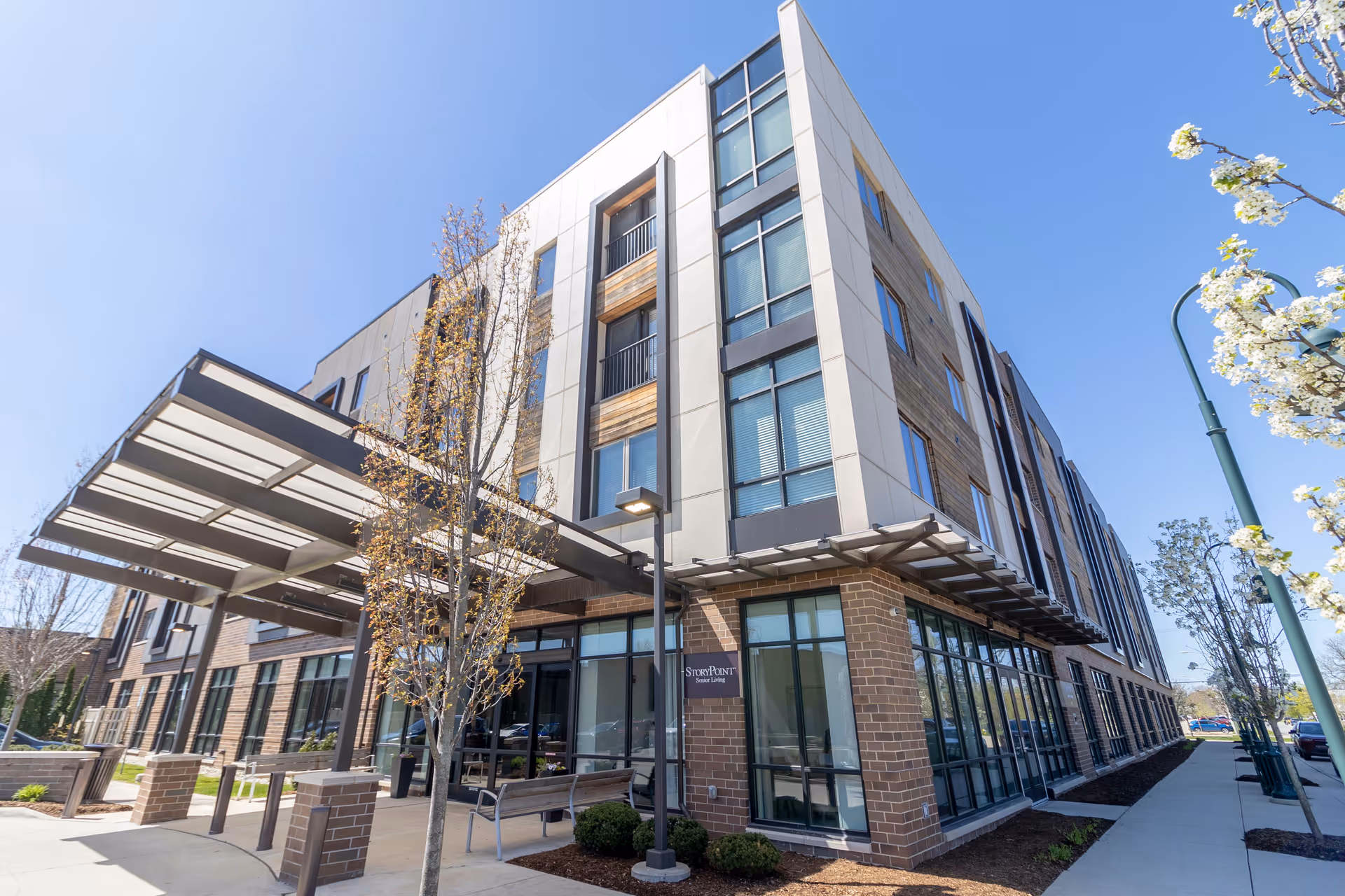 Exterior view of a modern multi-story senior living facility building named StoryPoint Birmingham with large windows, a covered entrance, and landscaped surroundings under a clear blue sky.
