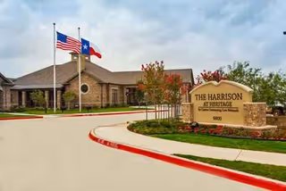 Exterior view of The Harrison at Heritage facility with sign, flags, and driveway