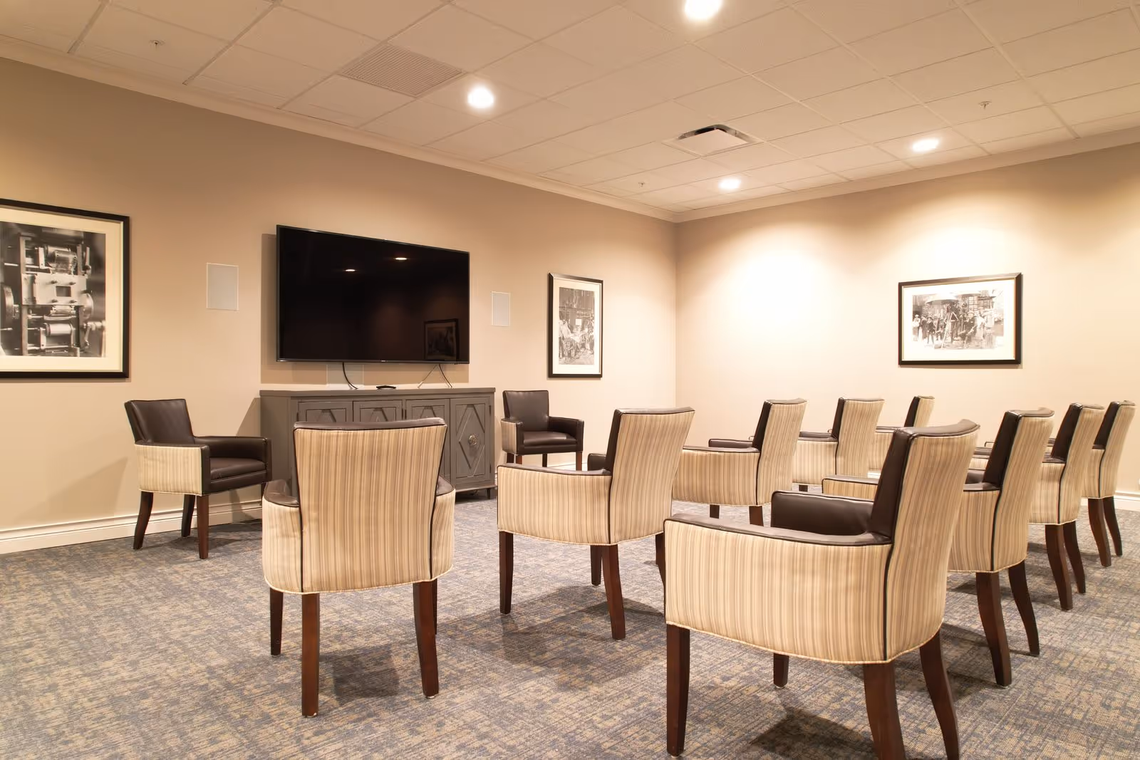 A senior common room with rows of upholstered chairs facing a wall-mounted flat-screen TV.