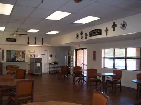 Interior communal dining area with round tables, chairs, and wall decor in a senior living center.