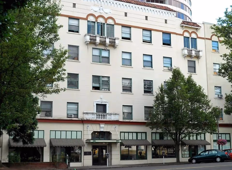 Exterior of a multi-story building with storefronts and trees.
