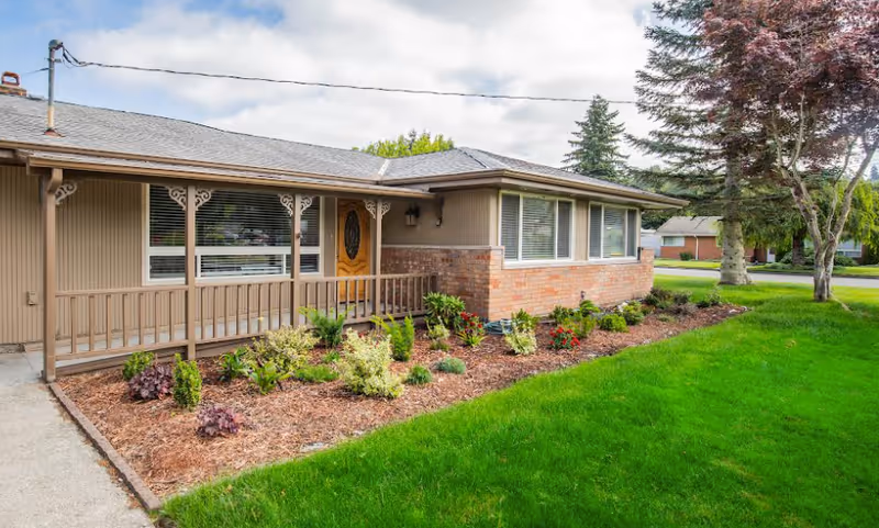 Single-story beige building with front porch, large windows, and landscaped lawn.