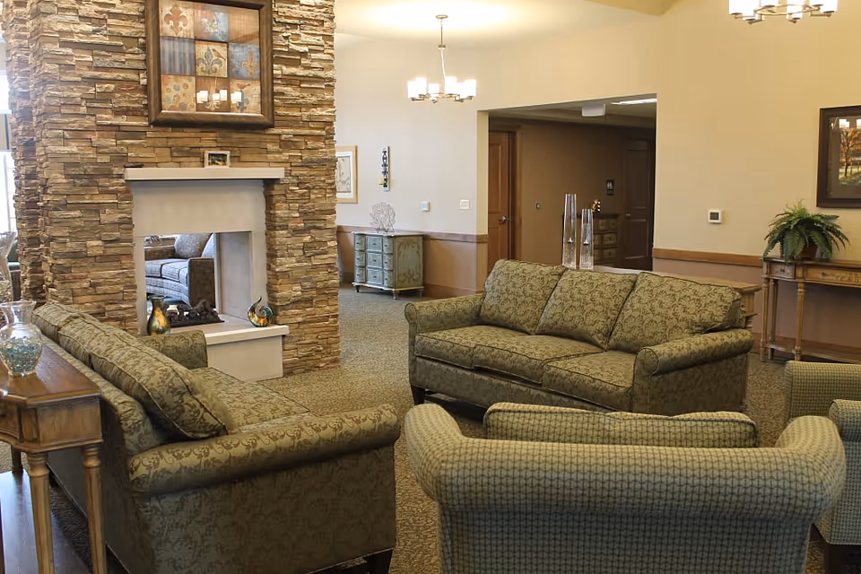 Comfortable sitting area in a senior living lounge with patterned sofas arranged around a double-sided stone fireplace.