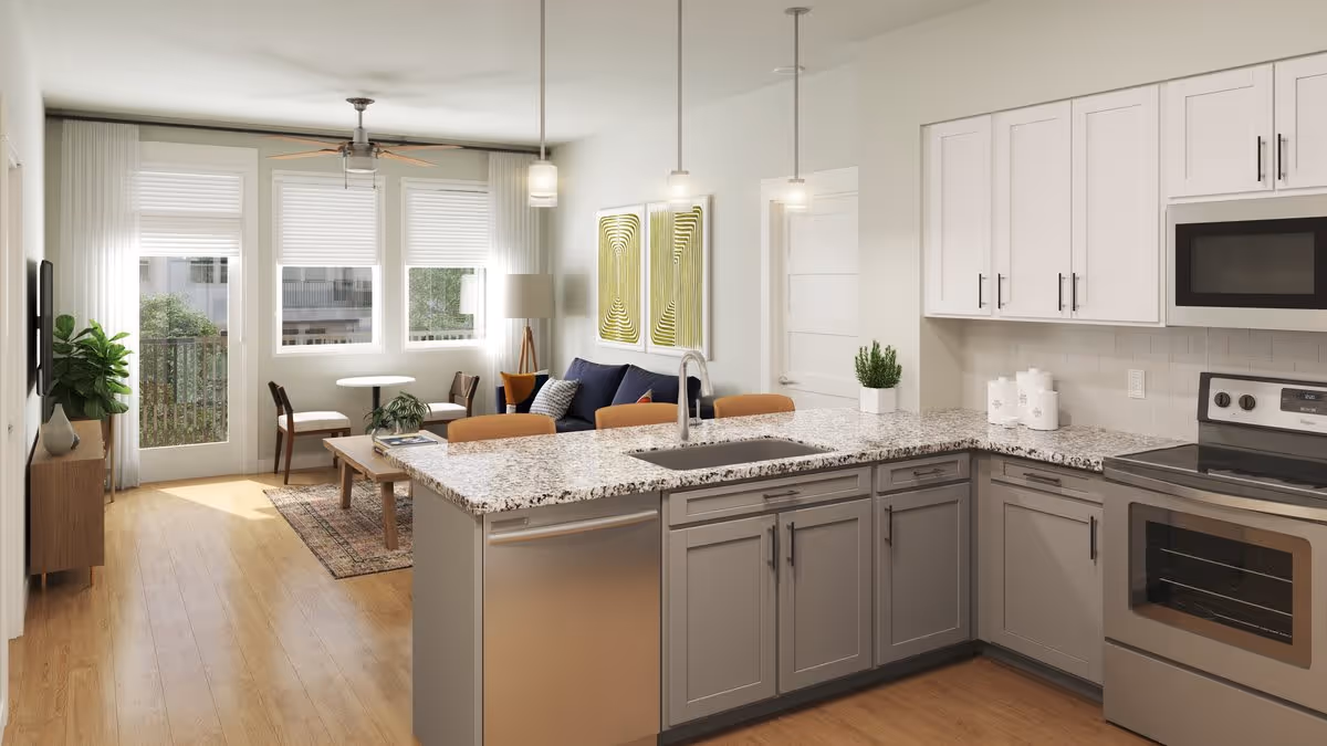 A modern open-concept living space featuring a kitchen with gray cabinets, granite countertops, stainless steel appliances, and a sink island with three pendant lights above. The living area includes a blue sofa, a wooden coffee table, two chairs around a small round table near windows, and a ceiling fan. The room has light wood flooring and large windows with white blinds allowing natural light to enter.