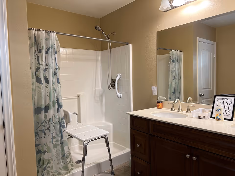 Bathroom with a walk-in shower featuring a shower chair and grab bar, and a vanity with sink and mirror.