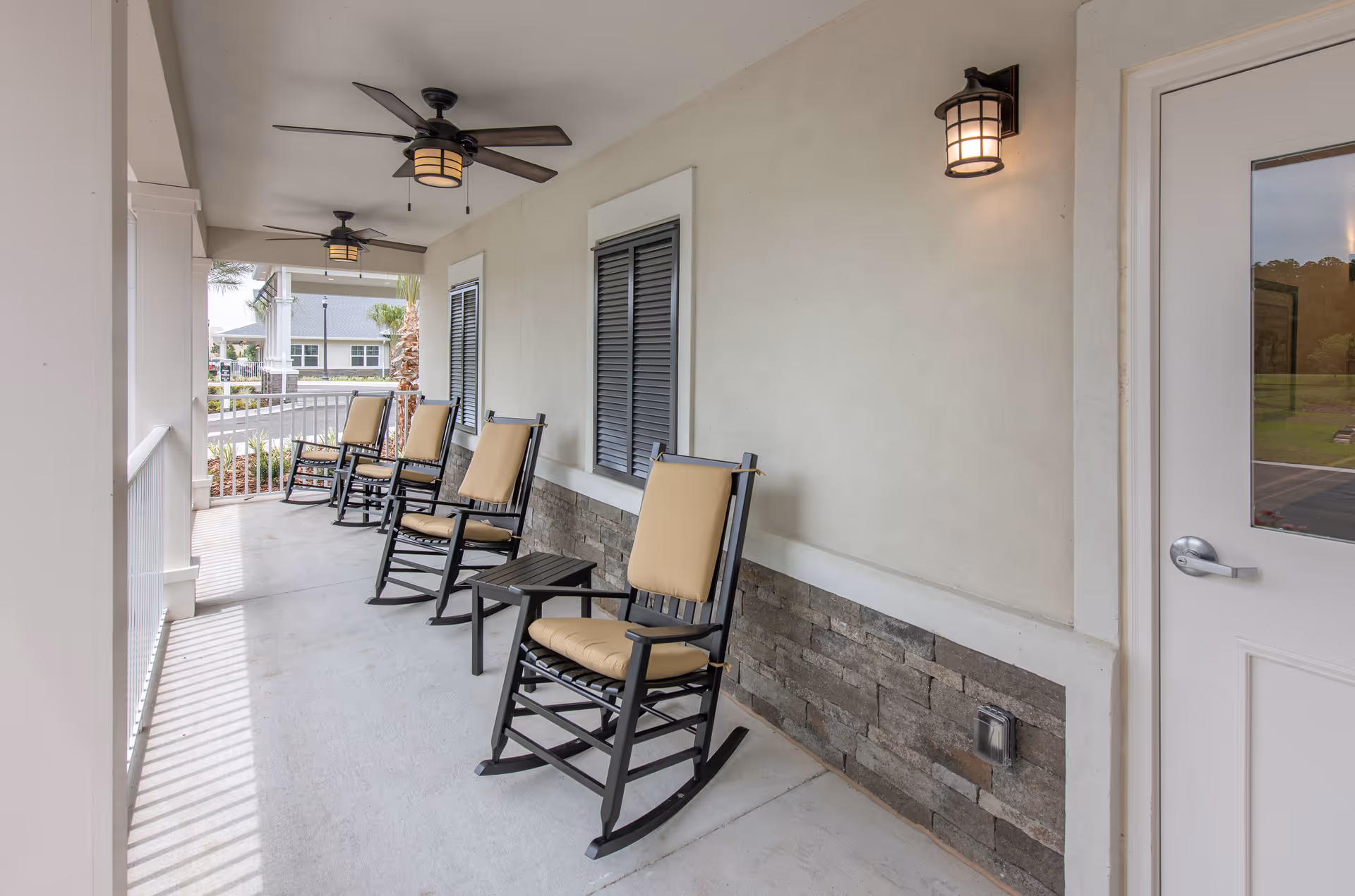Covered porch with several cushioned rocking chairs, ceiling fans, and outdoor lighting.