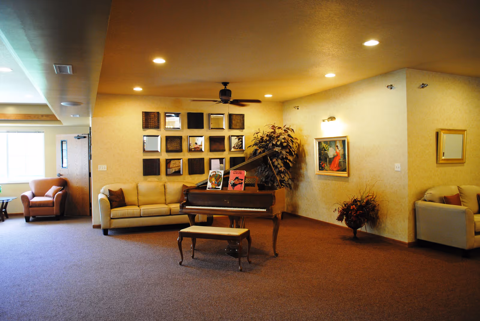 Spacious lounge area with a grand piano, sofas and armchairs, wall art, and warm recessed lighting.