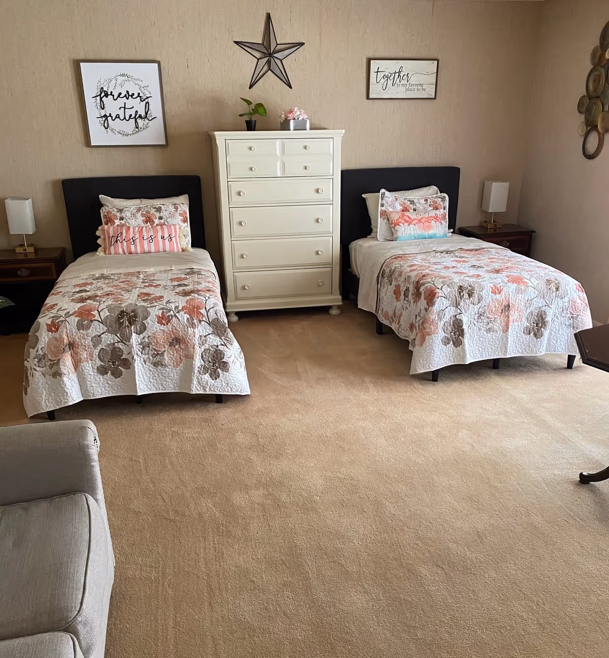 A softly decorated bedroom with two twin beds, a white dresser between them, floral bedspreads and wall decor.