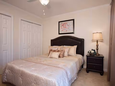 Neatly made bed with a dark headboard, nightstand and lamp in a softly lit bedroom.