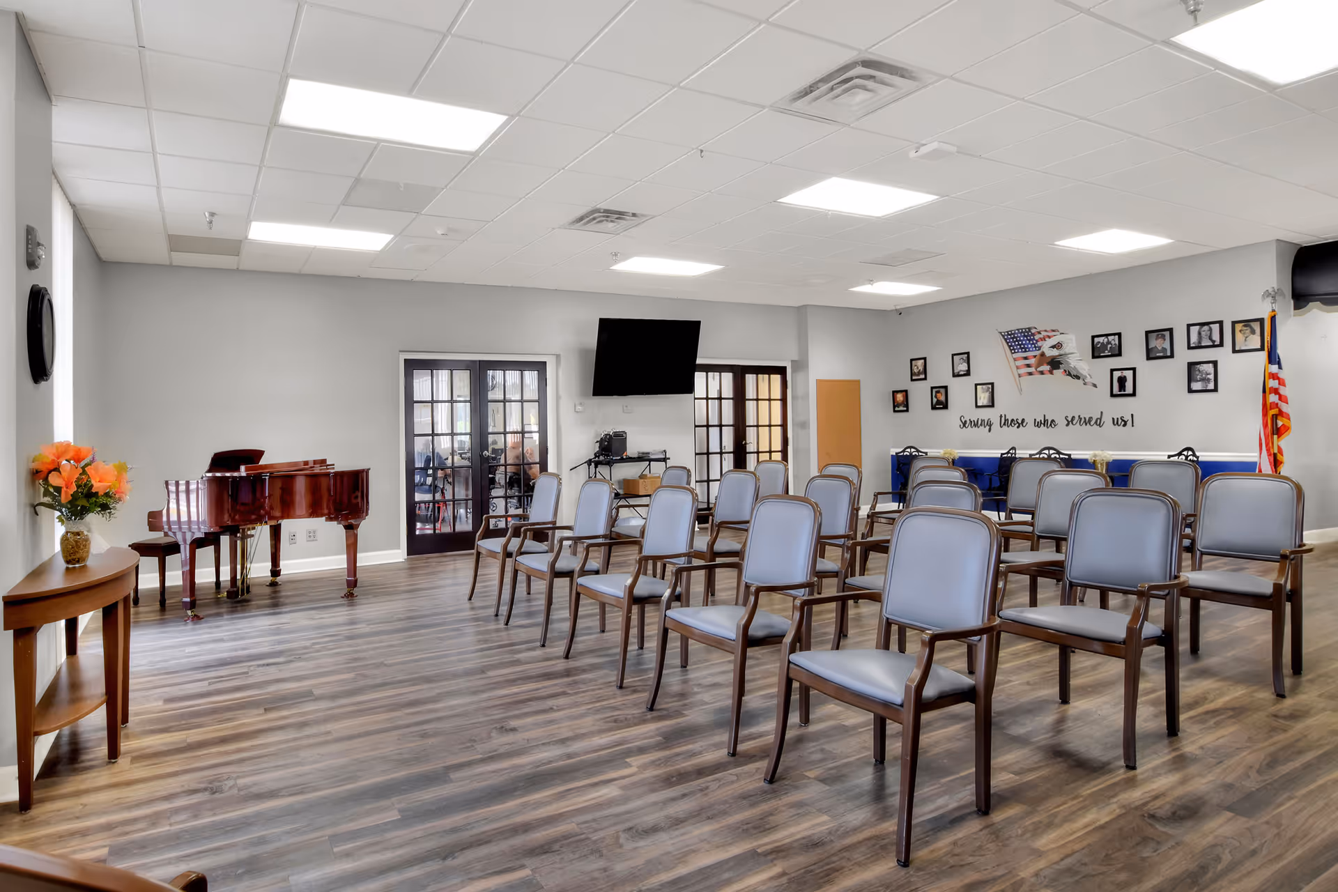 Bright multipurpose activity room with rows of chairs, a grand piano, wall photos, and an American flag.