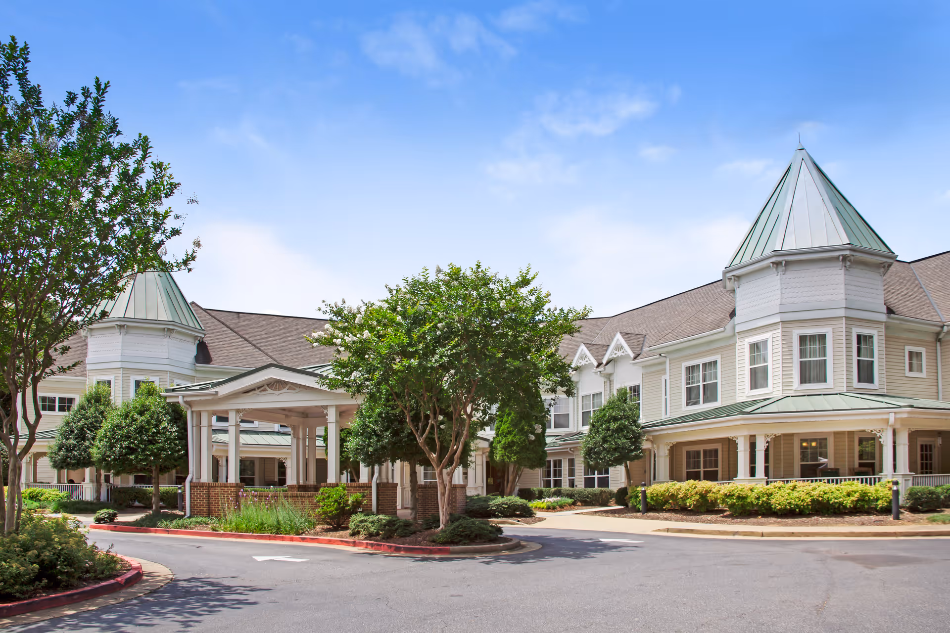 Front entrance and landscaped exterior of a large senior living building with turreted cupolas and a covered porte-cochere.