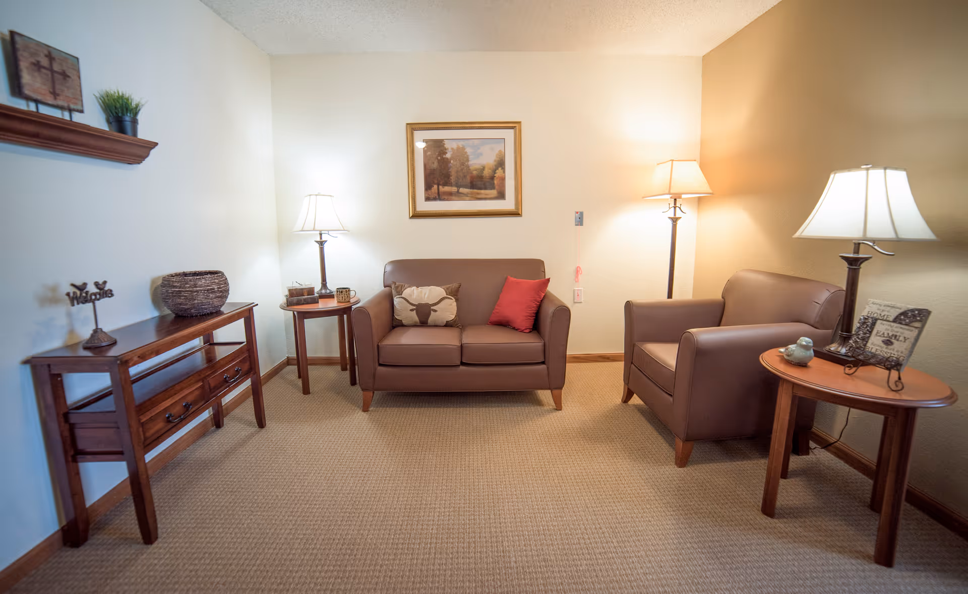 Small living room with a brown loveseat and armchair, side tables and lamps and a framed picture on the wall.