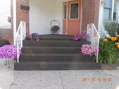 Front entry to a building with brick steps, pink door, and colorful flowers.