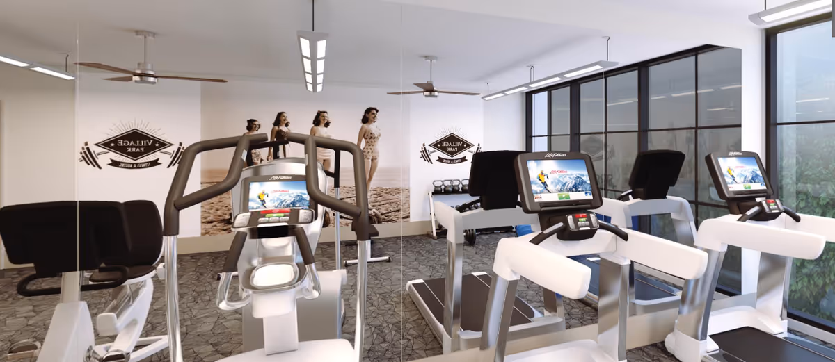 A modern fitness room with several treadmills and exercise bikes facing a mirrored wall. The room has large windows letting in natural light and wall art featuring vintage-style images of women in swimsuits and the Village Park logo.