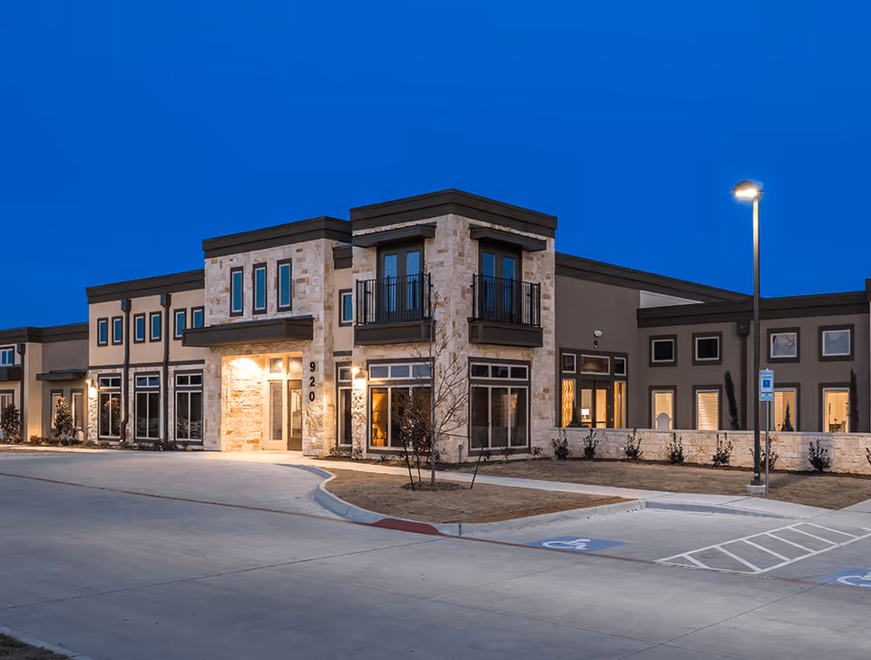 Front exterior view of The Heritage at Twin Creeks retirement community building at dusk.