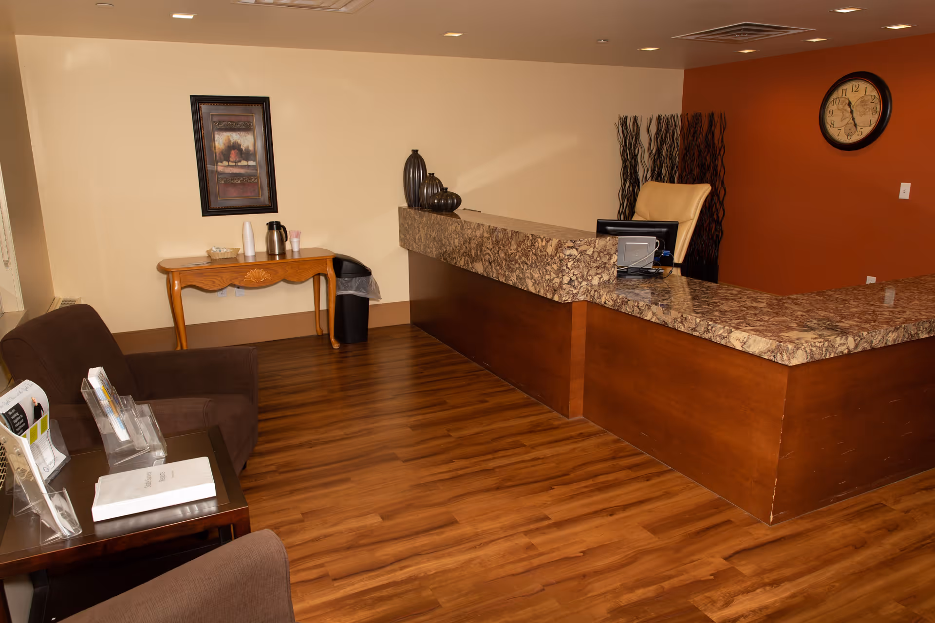 Reception area with a marble-topped front desk, seating, a small refreshment table and a wall clock.
