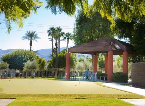 Outdoor courtyard with gazebo, palm trees, benches, and residents seated nearby.
