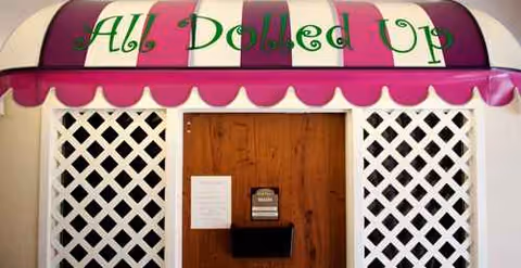 Front of a quaint shop with a pink striped awning, lattice panels, and a wooden door.