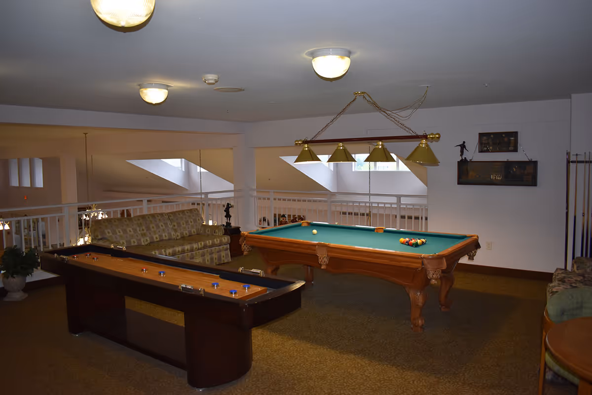 Interior game room with a pool table, shuffleboard table, couch seating and overhead lights.