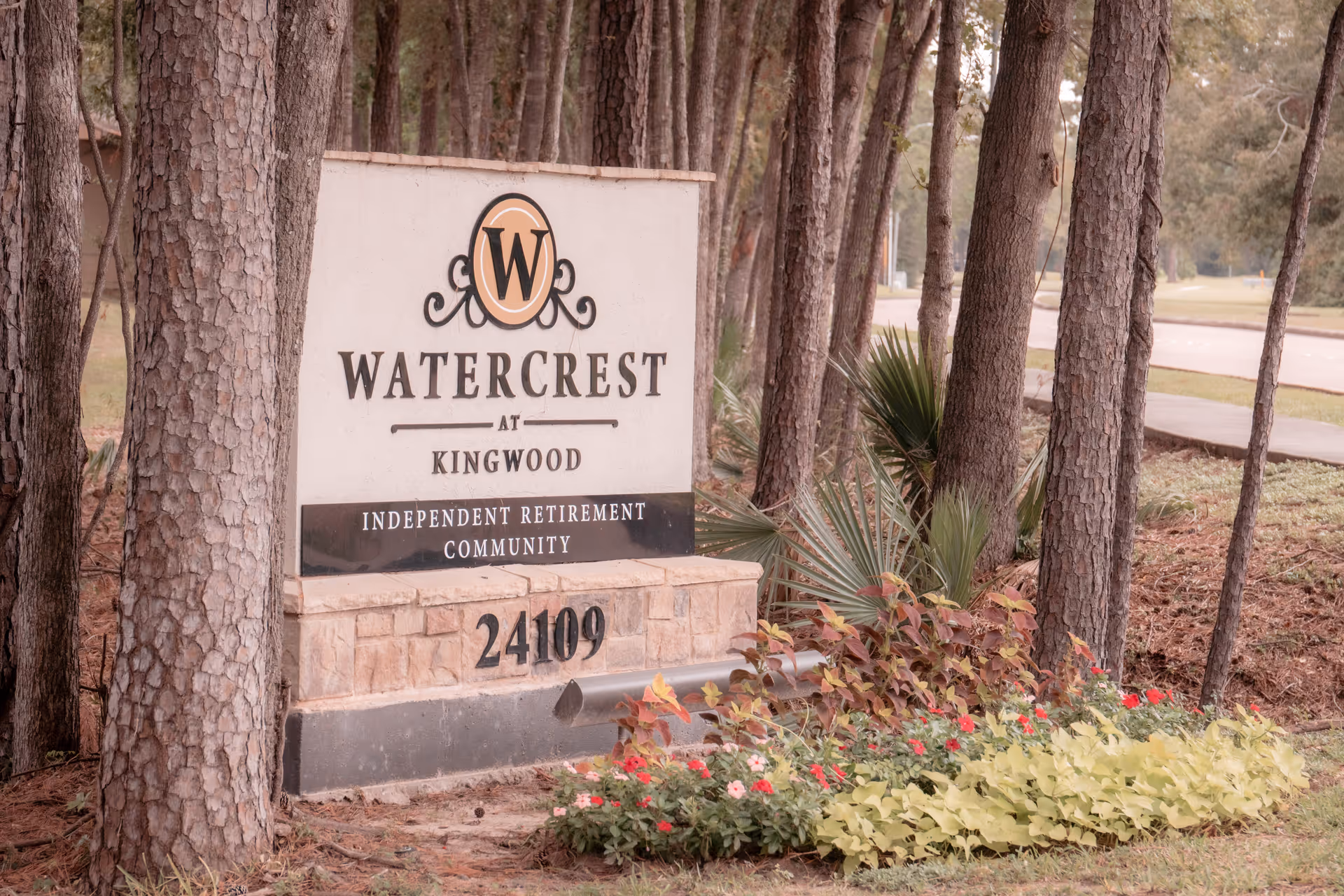 Entrance sign reading 'Watercrest at Kingwood Independent Retirement Community' surrounded by trees and landscaped flowers.