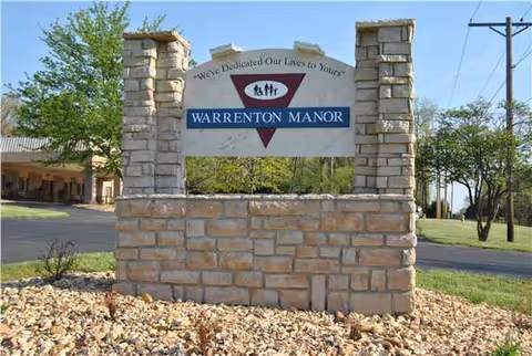 Stone entrance sign for Warrenton Manor with trees and landscaping.