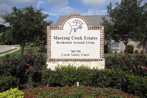 A brick-framed sign for Mustang Creek Estates Allen surrounded by landscaped bushes.