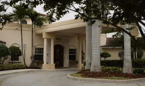 Exterior entrance of HarborChase of Tamarac with palm trees and a curved driveway
