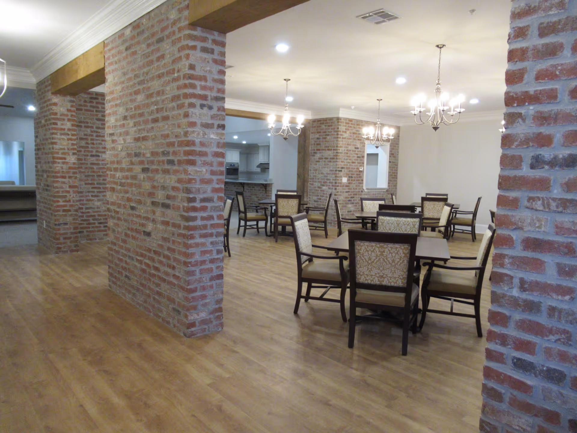Open dining room with wooden tables and upholstered chairs surrounded by exposed brick columns and chandeliers.