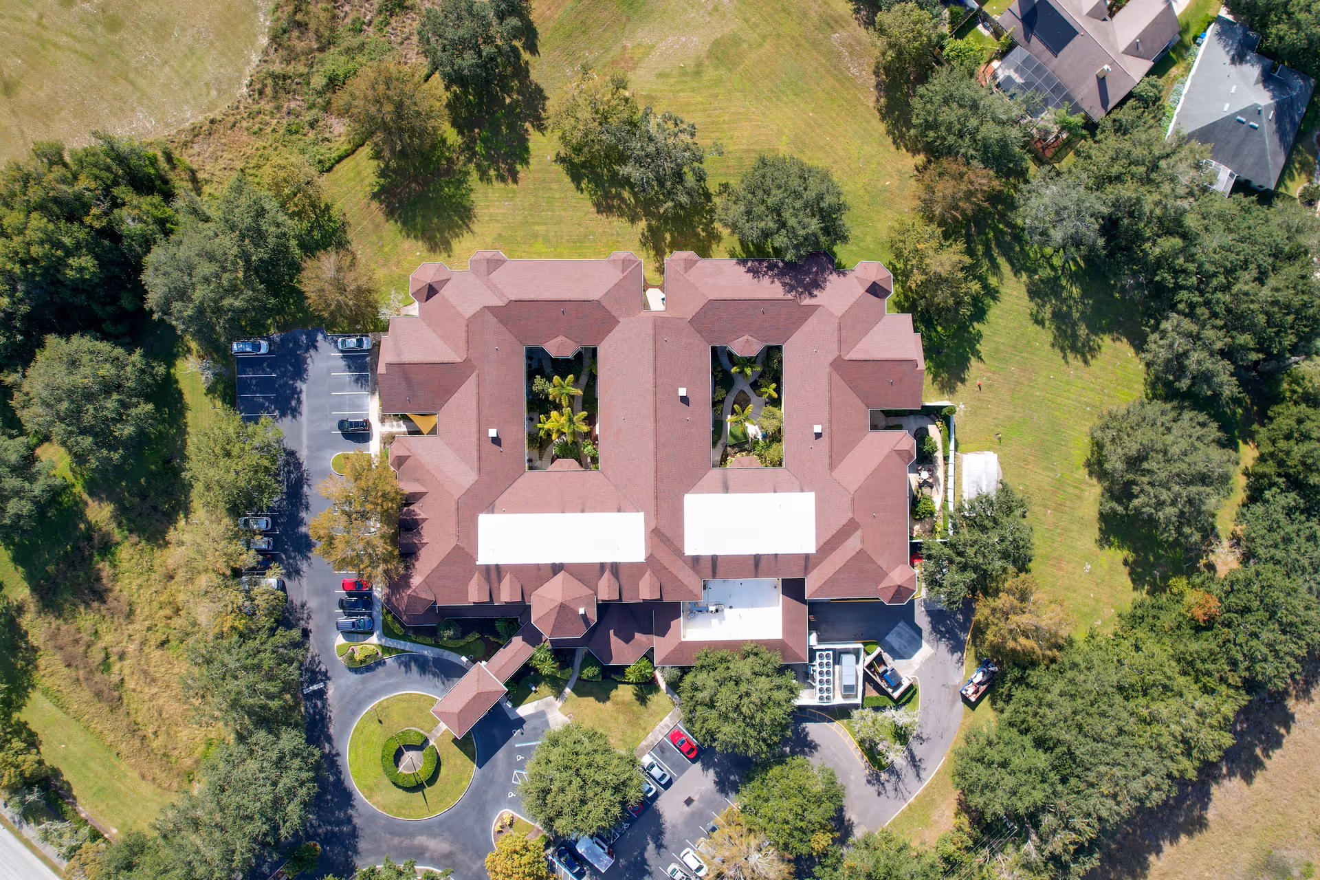 Aerial top-down view of a large red-roofed building with central courtyards, surrounding parking lots, trees, and lawns.