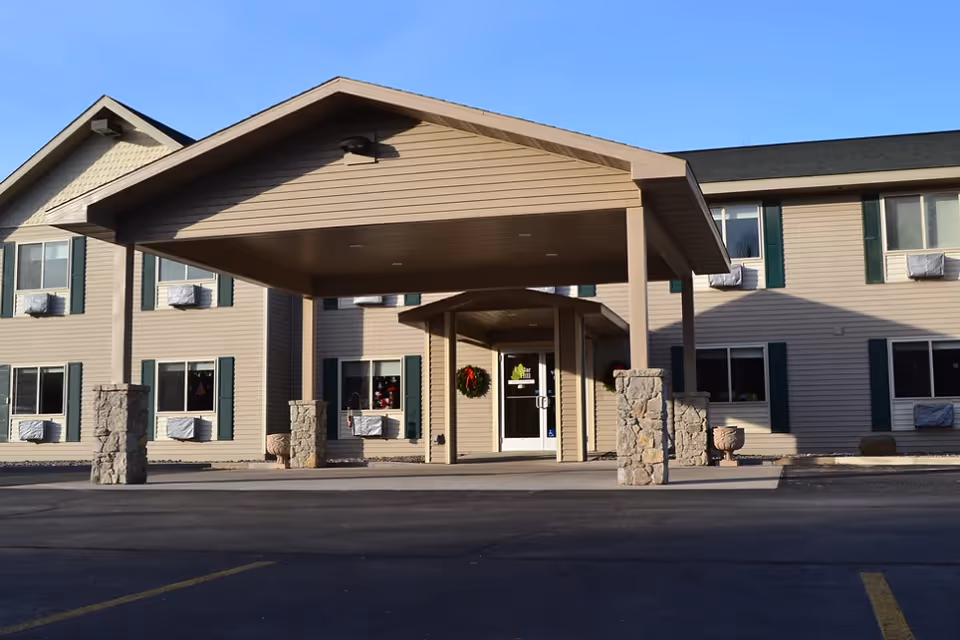 Front entrance of a senior living building with a covered drop-off canopy and a wreath on the glass door.