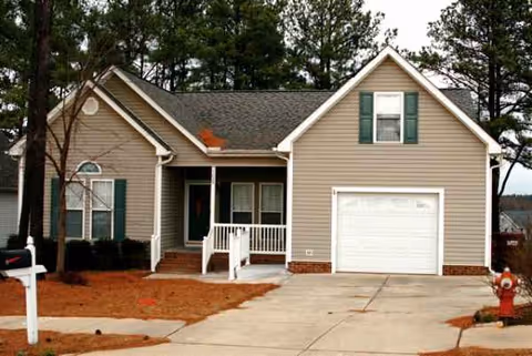 Residential single-family house with attached garage and front porch, pine trees in yard.