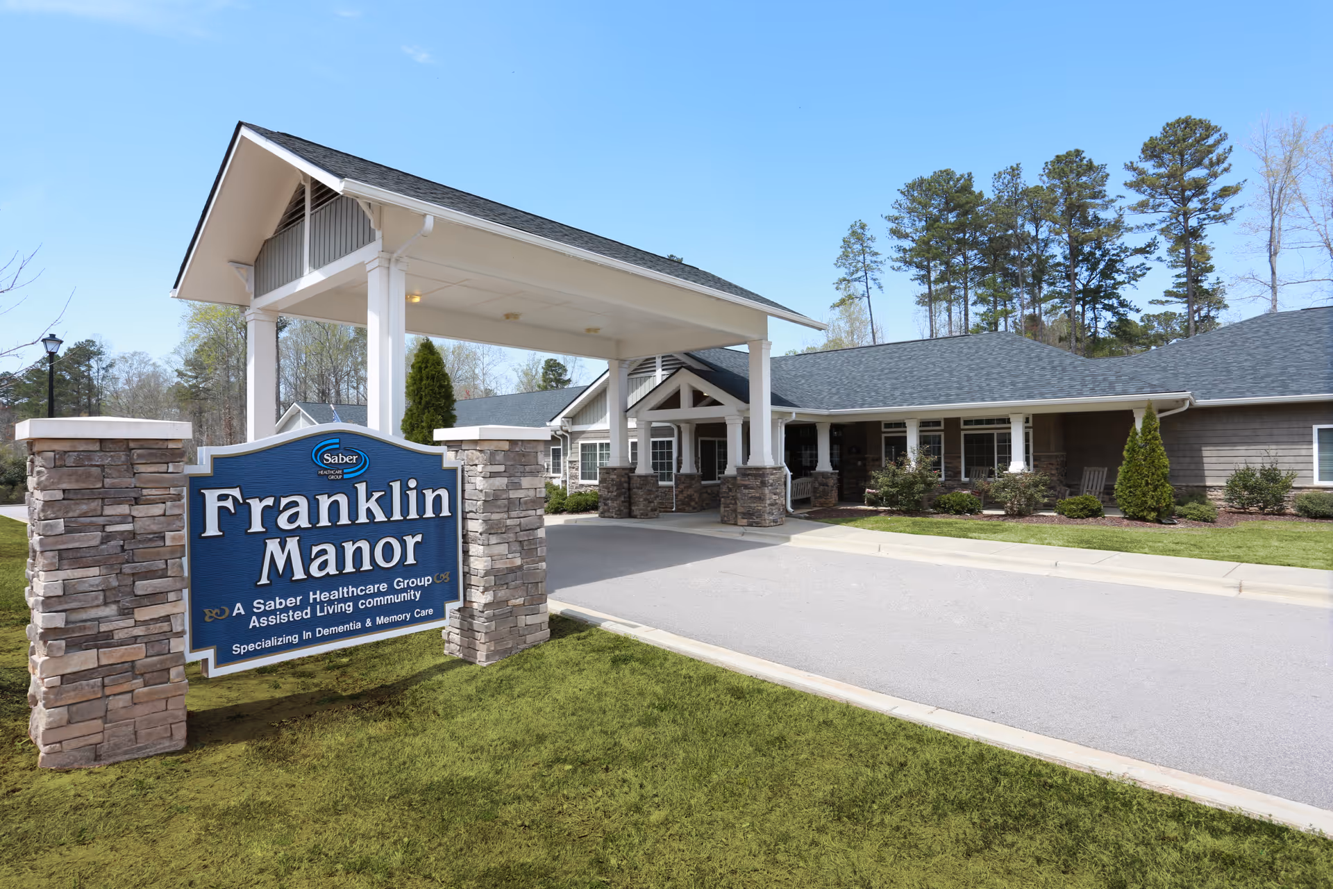 Front entrance and sign for Franklin Manor assisted living facility with a covered porte-cochère and landscaped grounds.