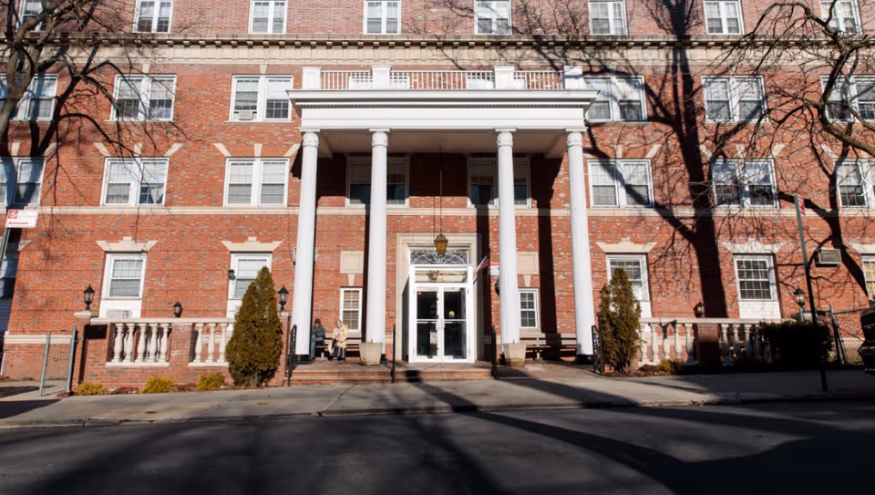Brick senior living facility with tall white columns and a central glass entrance.