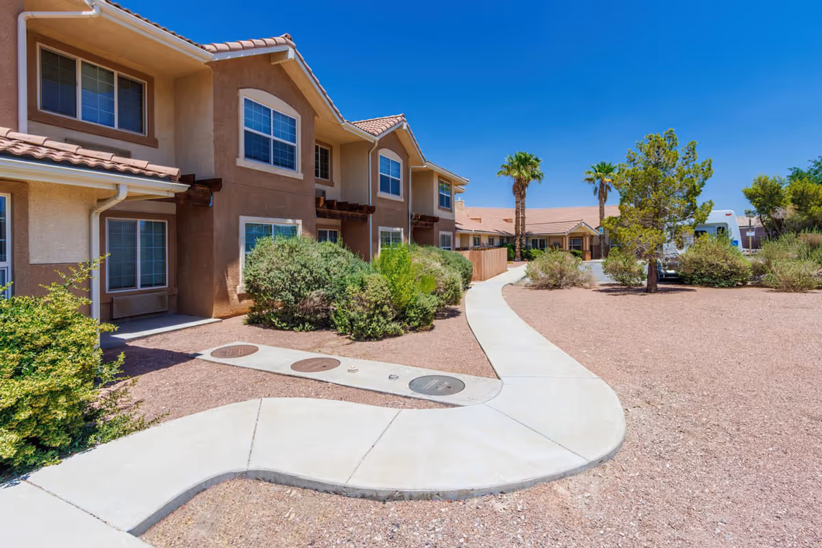 Exterior view of a two-story Parkway Assisted Living building with a curved concrete walkway, desert landscaping and palm trees under a clear blue sky.